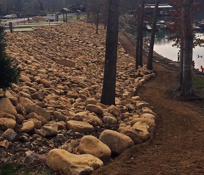 DeBord & Son Construction | stone work around a lake and trees creating a pathway along the shoreline